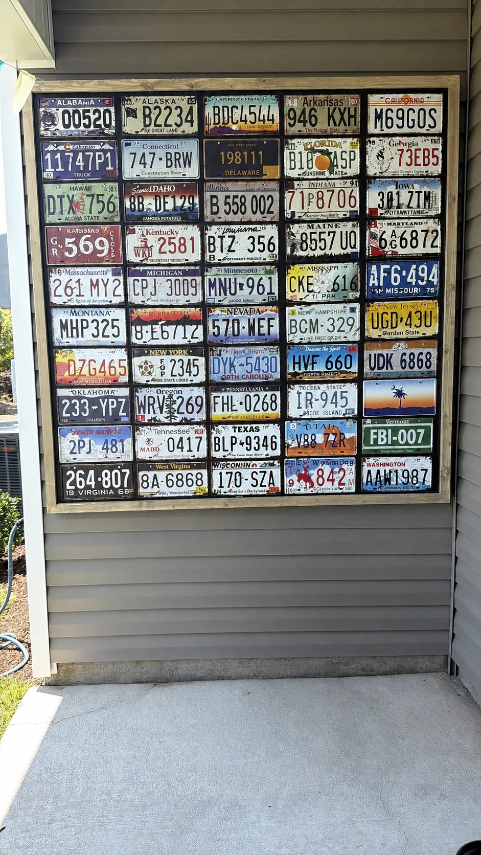 Custom framed collection of vintage license plates installed on an exterior wall